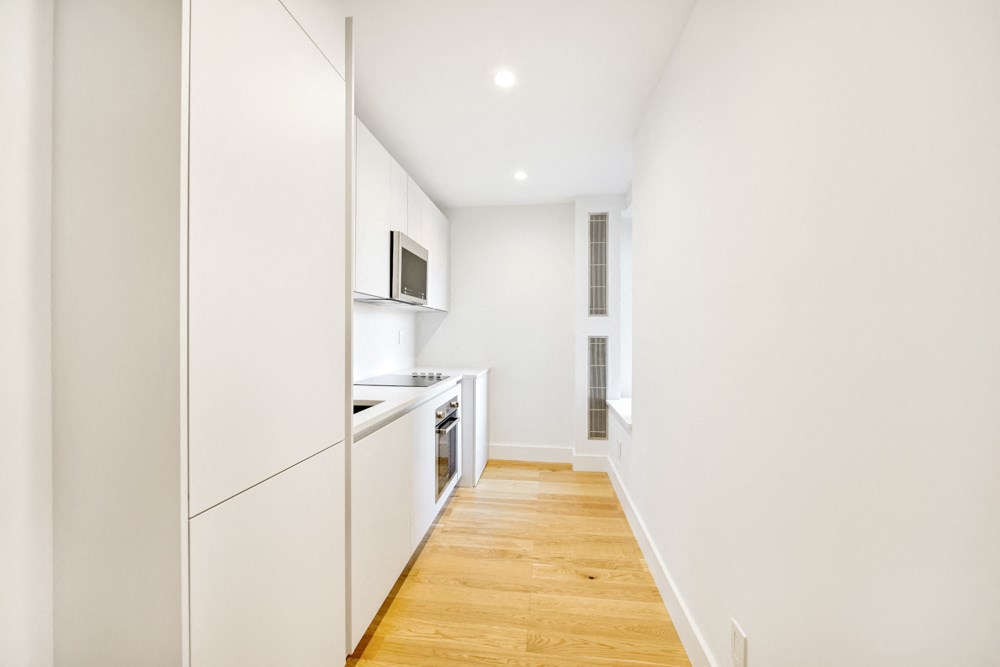 a long white kitchen with white cabinets and a wood floor